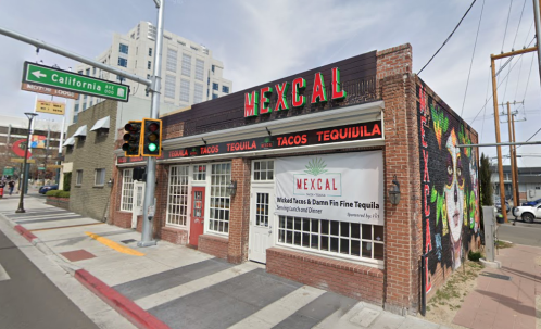 A colorful restaurant exterior featuring "Mexcal" signage, with a banner advertising tacos and tequila, near a traffic light.