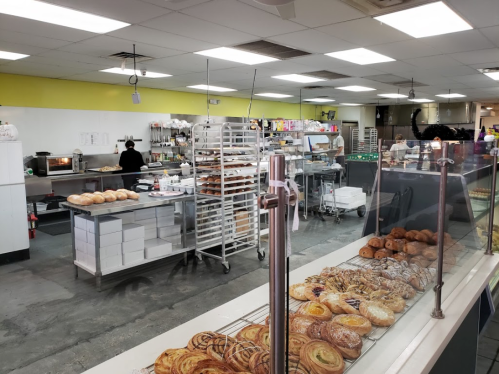 A bakery interior with shelves of pastries, a display case, and staff preparing food in the background.