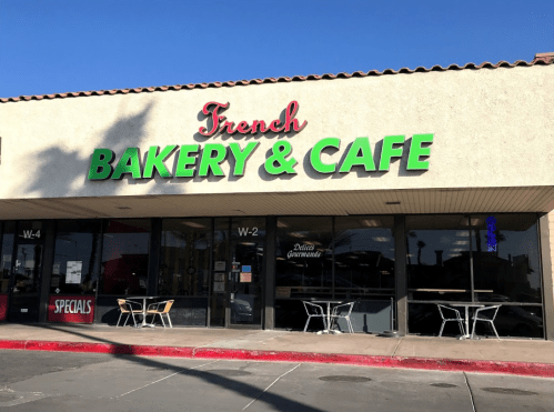 Exterior of a French bakery and café with a bright sign, featuring outdoor seating and a clear blue sky.