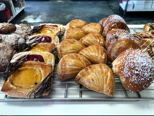 A variety of baked pastries on a cooling rack, including fruit tarts, flaky croissants, and sweet rolls.