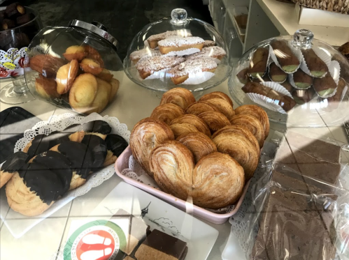 A display of assorted pastries, including croissants, cookies, and sweet rolls, under glass domes in a bakery.