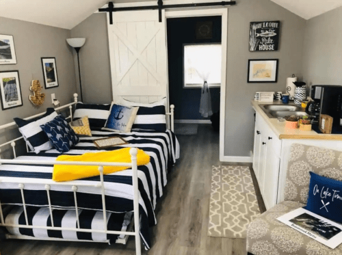 Cozy room with two daybeds, nautical decor, a kitchenette, and light gray walls. Bright and inviting atmosphere.