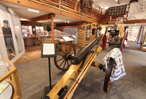 A museum interior featuring a wooden cannon, vintage fire engine, and various historical artifacts on display.