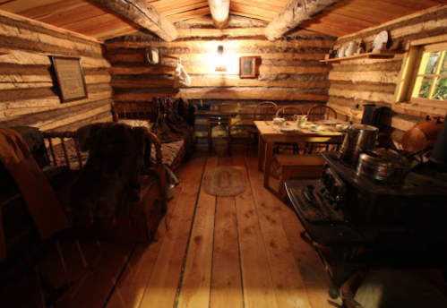 Cozy interior of a rustic log cabin with wooden furniture, a table set for meals, and a vintage stove.