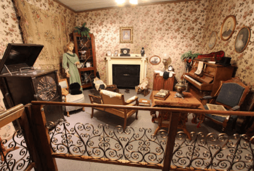 A vintage room with floral wallpaper, a piano, a mannequin, and antique furniture, creating a nostalgic atmosphere.