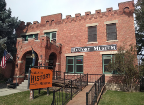 A brick building with a castle-like design, featuring a sign that reads "Gallatin History Museum" and an American flag.