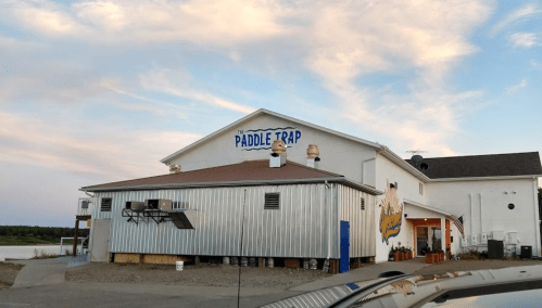 A building with the sign "The Paddle Trap," featuring a metal exterior and a scenic sky in the background.