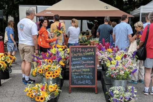 A vibrant farmers market scene with colorful flowers and a chalkboard listing fresh produce at M.M. Mullan Family Farm.