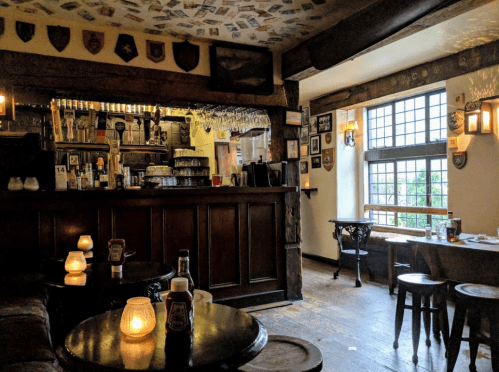 Cozy pub interior with a wooden bar, tables, candles, and vintage decor, featuring a window with a view outside.