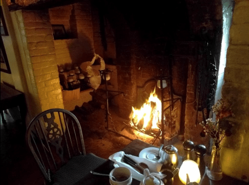 A cozy fireplace with a warm fire, surrounded by rustic decor and a table set for breakfast.