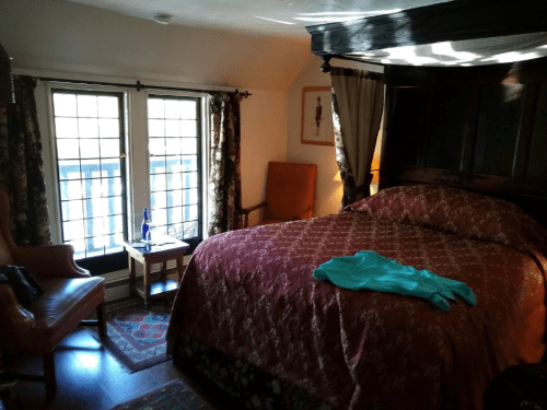 Cozy bedroom with a large bed, armchair, and a small table by the window, featuring warm colors and patterned decor.