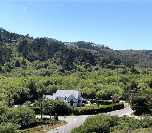 A scenic view of a house surrounded by lush greenery and trees, with a clear blue sky above.