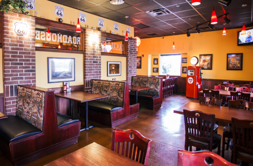Interior of a diner featuring booths, wooden tables, Route 66 decor, and a vintage gas pump. Warm, inviting atmosphere.