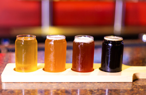 Four glasses of beer in a wooden flight, showcasing a range of colors from light yellow to dark black.