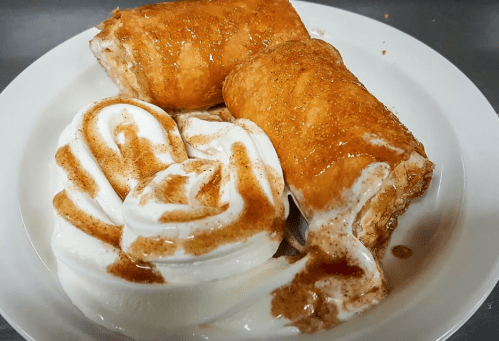 Two cinnamon rolls drizzled with syrup, served with a swirl of whipped cream on a white plate.