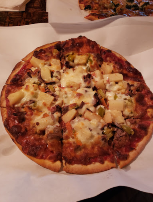 A pizza topped with cheese, pineapple, green peppers, and chunks of meat, cut into slices on a white paper.
