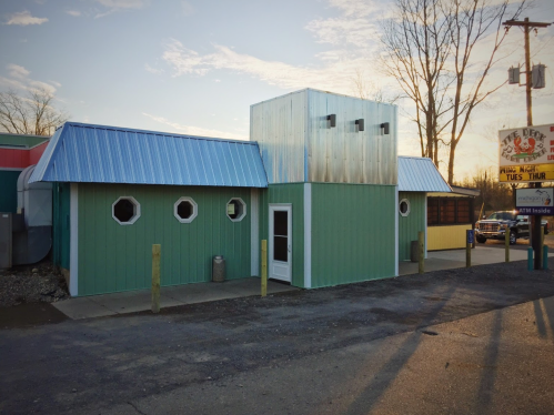 A green building with a blue roof and unique windows, set against a clear sky during sunset.