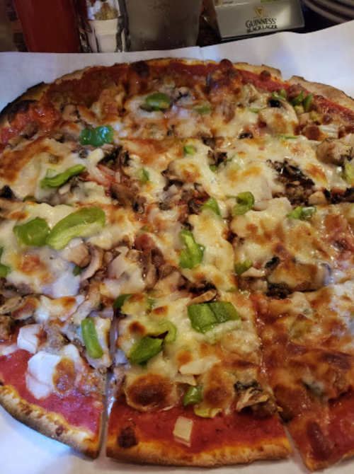 A close-up of a pizza topped with cheese, green peppers, onions, and mushrooms, served on a white plate.