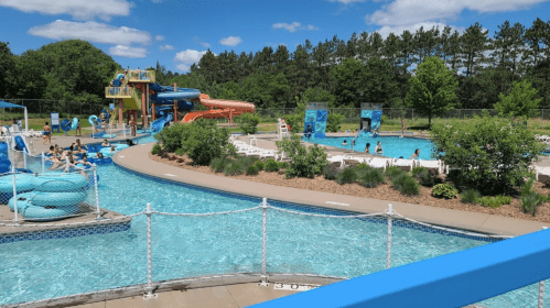 A vibrant water park scene with slides, pools, and people enjoying the sunny day surrounded by greenery.