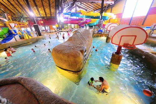 A vibrant indoor water park with slides, a rock feature, and families enjoying the water.