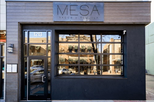Exterior of MESA Tacos + Tequila restaurant, featuring large windows and a modern wooden facade. Address: 1213.