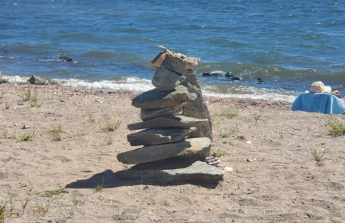 A stack of smooth stones on a sandy beach, with water and a person in the background.