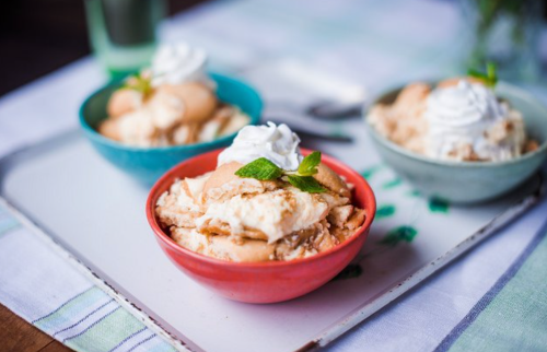 Three bowls of dessert with whipped cream and mint leaves, served on a tray with a striped cloth underneath.