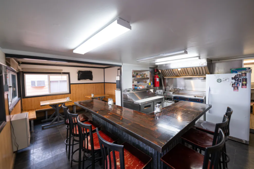 A modern kitchen with a large wooden counter, bar stools, and stainless steel appliances, featuring bright overhead lights.