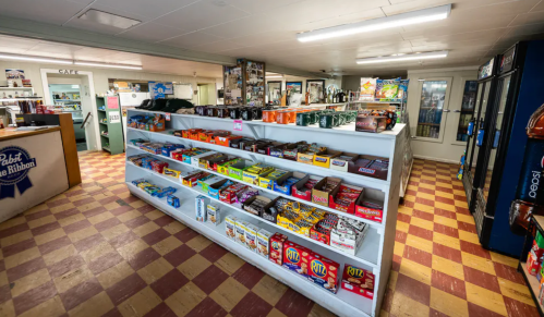 A view of a small store interior with shelves stocked with snacks and drinks, featuring a checkered floor.