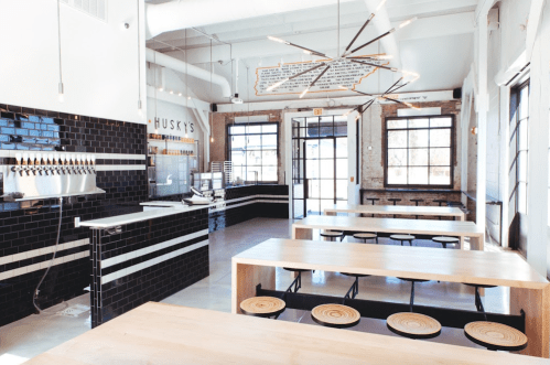 Modern interior of a restaurant with wooden tables, black tiles, and a unique light fixture. Bright and spacious atmosphere.