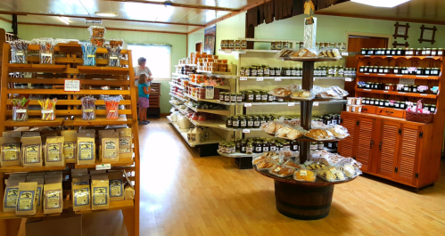 A cozy store interior filled with shelves of jars, baked goods, and snacks, with customers browsing in the background.