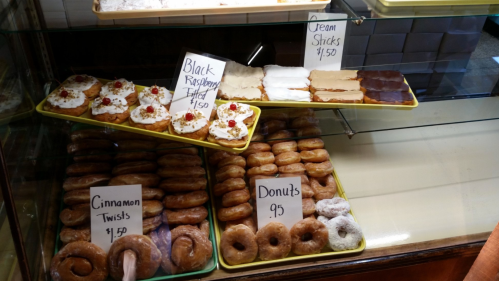 A display case filled with various pastries, including donuts, cinnamon twists, and black raspberry filled treats.