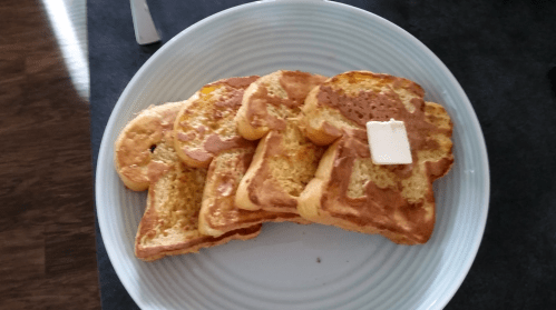 A plate of four golden-brown French toast slices, topped with a pat of butter.