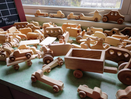 A collection of various wooden toy vehicles scattered on a table, with a window in the background.
