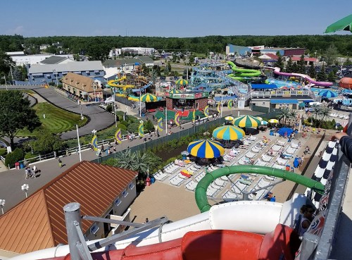 Aerial view of a vibrant water park with slides, pools, and colorful umbrellas on a sunny day.