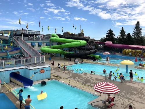 A vibrant water park with slides, pools, and families enjoying a sunny day. Colorful umbrellas and flags decorate the scene.