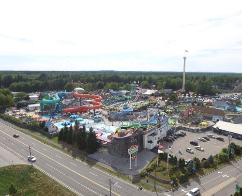 Aerial view of a vibrant water park with slides, pools, and attractions, surrounded by trees and a road.