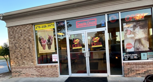 Exterior of Dazzle Dogs restaurant with large glass doors, colorful signage, and a welcoming "OPEN" sign.