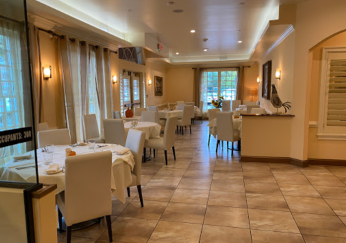 A spacious, elegantly decorated restaurant with white tables and chairs, soft lighting, and large windows.