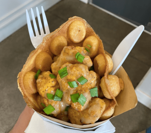 A waffle cone filled with chicken pieces in a creamy sauce, topped with green onions and surrounded by mini waffles.