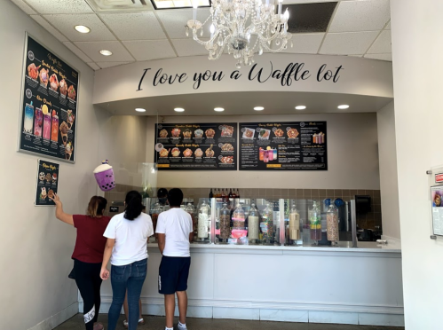 A dessert shop interior with a menu, customers ordering, and a sign that says "I love you a Waffle lot."