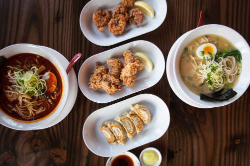 A table spread featuring ramen, fried chicken, and dumplings, garnished with lemon and green onions.