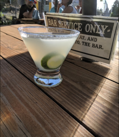 A refreshing cocktail with lime slices sits on a wooden table next to a sign that reads "BAR SERVICE ONLY."