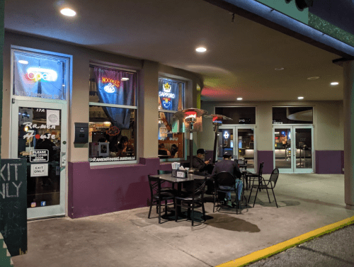 Exterior of a ramen restaurant at night, featuring outdoor seating and illuminated signs. Two people are seated at a table.