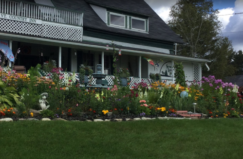 A charming inn with a vibrant flower garden in front, featuring colorful blooms and decorative elements.