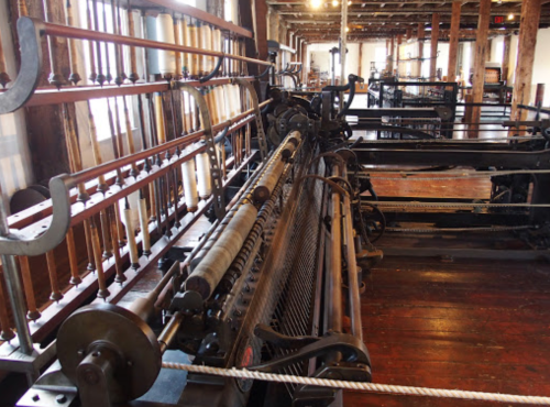 Historic textile machinery in a spacious workshop, showcasing intricate gears and mechanisms.