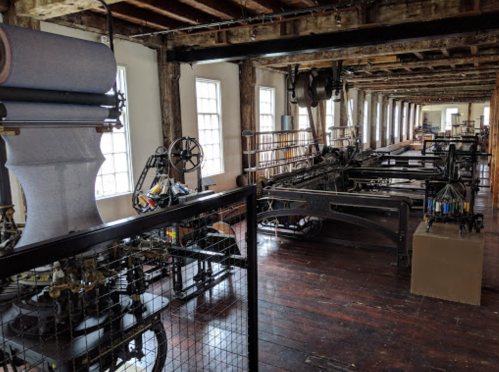 Interior of a historic workshop featuring large, vintage machinery and wooden beams, with natural light streaming in.