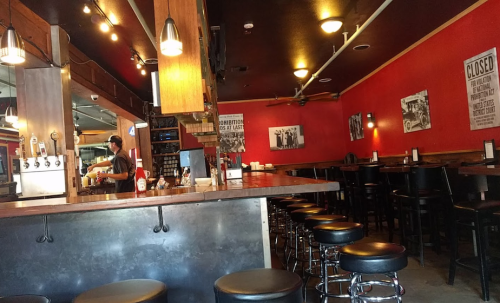 A cozy restaurant interior with red walls, bar stools, and a bartender preparing drinks in the background.