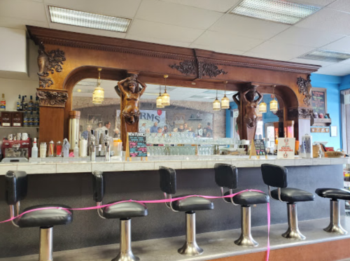 A vintage-style bar with ornate wooden details and black stools, featuring decorative figures and a colorful backdrop.