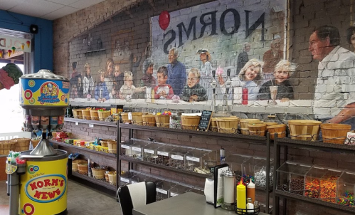 A colorful candy dispenser in front of a mural depicting a lively gathering of people in a cozy shop.